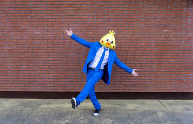 Mann in leuchtend blauem Anzug und Vogelmaske posiert auf einem Bein vor einer Backsteinmauer - OIPF00776