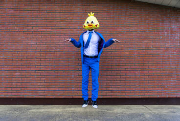 Man wearing vibrant blue suit and bird mask pretending to fly in front of brick wall - OIPF00777