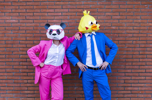 Mann und Frau in farbenfrohen Anzügen und Tiermasken posieren zusammen vor einer Backsteinmauer - OIPF00779