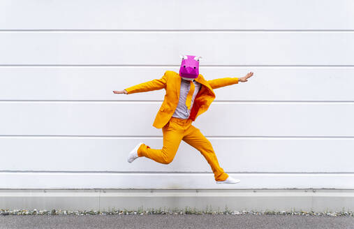 Mann in leuchtend orangefarbenem Anzug und Nilpferdmaske springt vor eine weiße Wand - OIPF00799