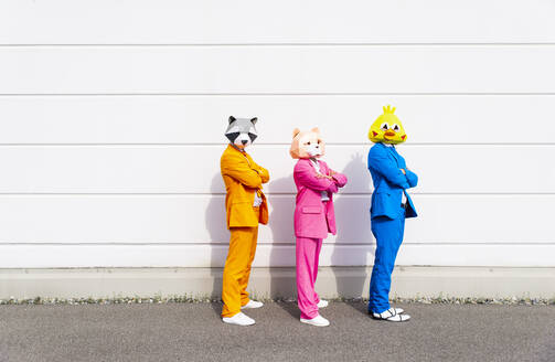 Drei Menschen in farbenfrohen Anzügen und Tiermasken posieren nebeneinander vor einer weißen Wand - OIPF00805