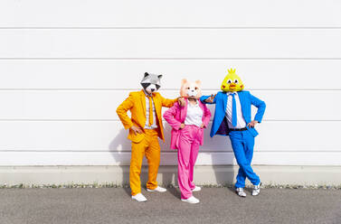 Three people wearing vibrant suits and animal masks posing side by side in front of white wall - OIPF00806