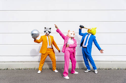 Three people wearing vibrant suits and animal masks partying in front of white wall - OIPF00807