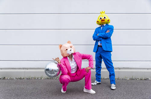 Mann und Frau in farbenfrohen Anzügen und Tiermasken posieren mit Discokugel vor einer weißen Wand - OIPF00808