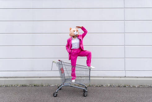 Frau in leuchtend rosa Anzug und Bärenmaske steht in einem Einkaufswagen - OIPF00811