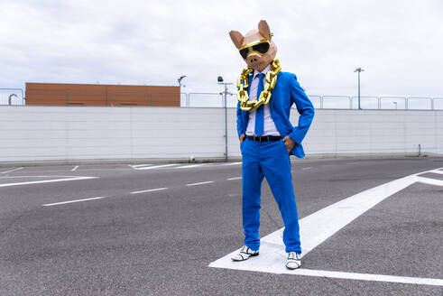 Lustige Figur mit Tiermaske und blauem Geschäftsanzug, die sich auf einem leeren Parkplatz amüsiert - OIPF00822