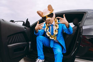 Lustige Figur in Tiermaske und blauem Geschäftsanzug sitzt im Auto und gestikuliert - OIPF00828