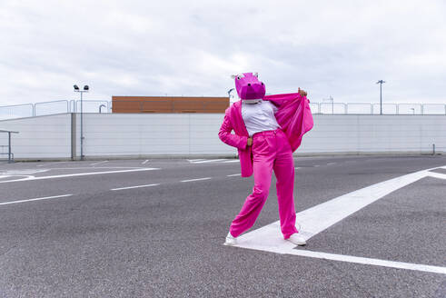 Lustige Figur mit Tiermaske und rosa Business-Anzug, die sich auf einem leeren Parkplatz amüsiert - OIPF00830