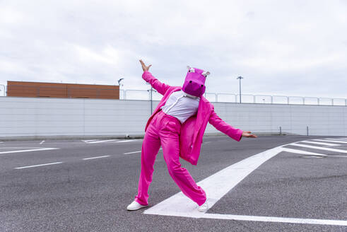 Lustige Figur mit Tiermaske und rosa Business-Anzug, die sich auf einem leeren Parkplatz amüsiert - OIPF00831
