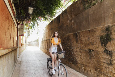 Smiling woman cycling in alley - JRVF00762