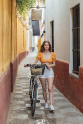 Junge Frau mit Fahrrad in einer Gasse - JRVF00764