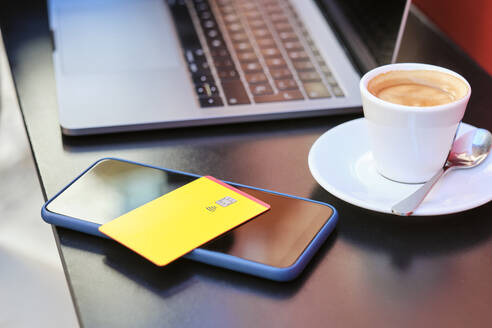 credit card on smart phone by coffee cup and laptop at sidewalk cafe - AODF00496