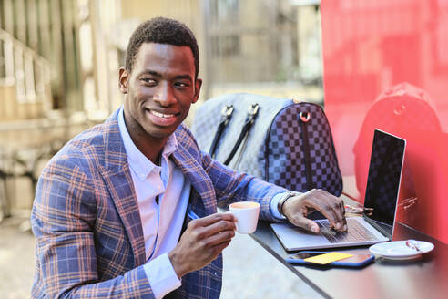 Smiling businessman with coffee cup sitting at sidewalk cafe - AODF00497