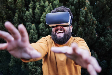 Playful man using VR glasses in garden - ASGF00316