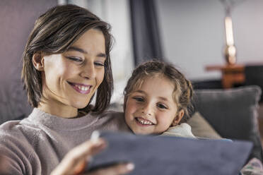 Smiling mother and daughter using digital tablet at home - AUF00610
