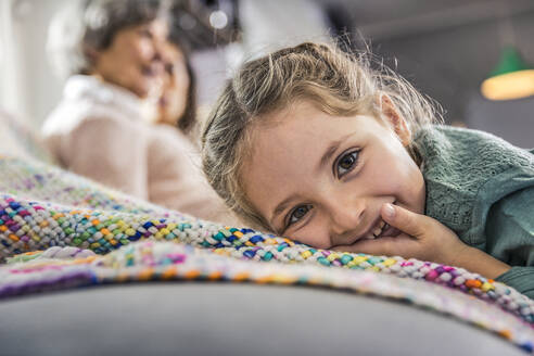 Smiling girl leaning on sofa with women in background at home - AUF00614