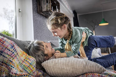 Grandmother playing with granddaughter while lying on sofa at home - AUF00617