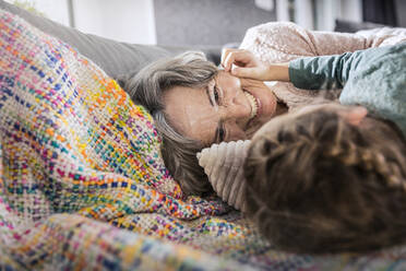 Girl and senior woman smiling while lying on sofa at home - AUF00618