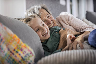 Happy grandmother and granddaughter resting on sofa in living room - AUF00619