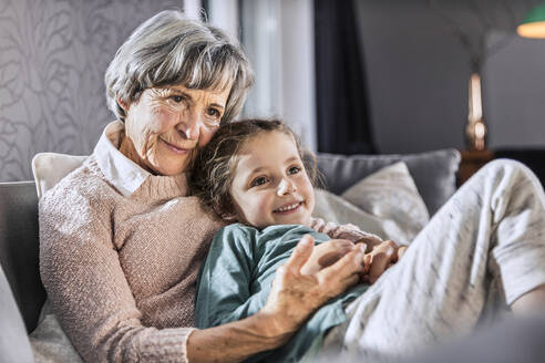 Mädchen entspannt sich mit älterer Frau auf Sofa im Wohnzimmer - AUF00621