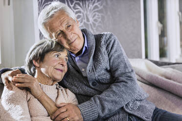 Senior man sitting with arm around on woman in living room - AUF00622