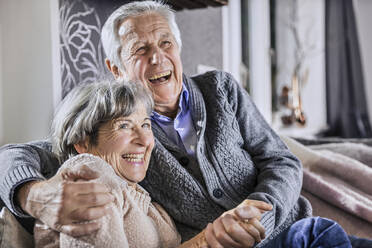 Senior couple holding hands while sitting together in living room - AUF00624