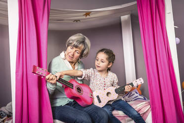 Granddaughter teaching about guitar to grandmother in bedroom - AUF00628