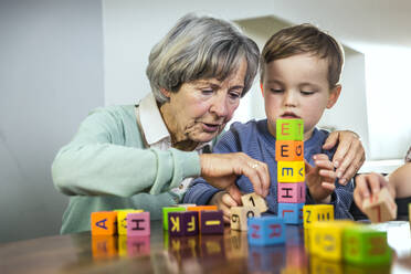 Grandmother helping grandson stacking toy blocks at home - AUF00646