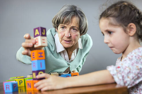 Ältere Frau stapelt Spielzeugblock beim Spielen mit Mädchen zu Hause - AUF00650