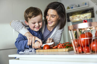 Mother teaching son to cut tomato on cutting board at kitchen - AUF00651