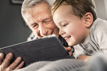 Smiling boy using digital tablet with senior man at home - AUF00657