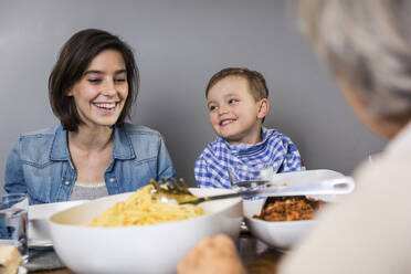 Lächelnde Mehrgenerationenfamilie beim Essen zu Hause - AUF00663