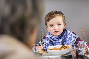 Ältere Frau mit Junge im Hintergrund beim Essen zu Hause - AUF00667