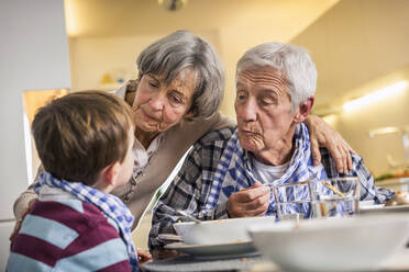 Großeltern sehen ihren Enkel an, während sie zu Hause essen - AUF00671