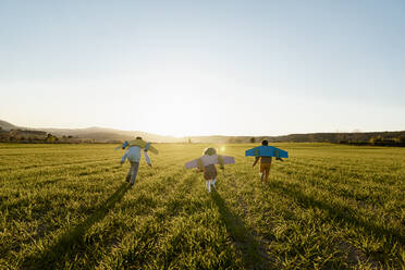 Playful brothers and sister with rocket wings running on agricultural field during sunny day - RCPF01091