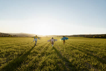 Brothers and sister with rocket wings running on agricultural field during sunny day - RCPF01092