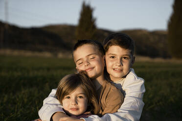 Brother and sister sitting with arms around at agricultural field - RCPF01096