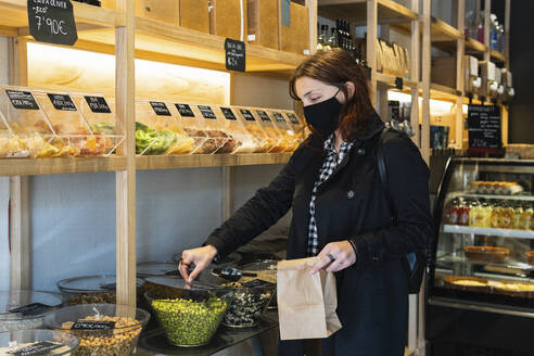 Frau mit Gesichtsschutz beim Kauf von grünen Erbsen im Supermarkt während der Pandemie - PNAF01605