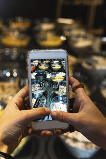 Junge Frau fotografiert Lebensmittel mit dem Mobiltelefon in einem Einzelhandelsgeschäft - PNAF01619