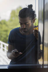 Männlicher Berufstätiger, der in der Pause im Büro eine SMS über sein Smartphone verschickt - BMOF00760