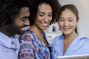 Lächelnde männliche und weibliche Fachkräfte, die auf ein digitales Tablet schauen, während sie sich im Büro unterhalten - BMOF00780