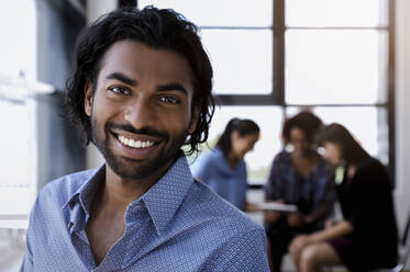 Smiling young businesswoman standing while female colleagues discussing in office - BMOF00784