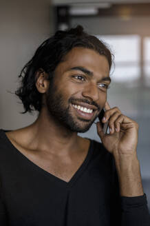 Lächelnder männlicher Unternehmer, der im Büro mit dem Handy telefoniert und dabei wegschaut - BMOF00789