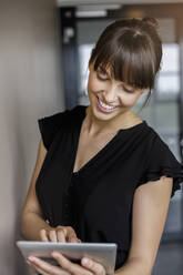 Young smiling businesswoman with bangs using digital tablet in office - BMOF00792