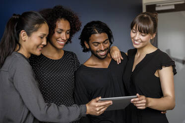Lächelnder männlicher und weiblicher Unternehmer, die sich ein digitales Tablet teilen, während sie sich im Büro unterhalten - BMOF00794