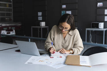 Weibliche Fachkraft mit Brille schreibt im Büro in ein Tagebuch - PNAF01658