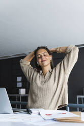 Businesswoman with hands behind head relaxing at office - PNAF01664