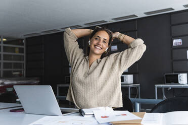 Smiling businesswoman with hands behind head sitting at desk in office - PNAF01665