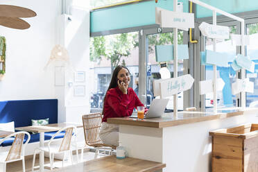 Lächelnde weibliche Fachkraft, die in einem Restaurant mit ihrem Handy telefoniert - PNAF01675