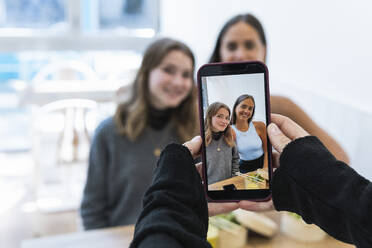 Älterer Mann fotografiert Freundinnen mit dem Handy im Restaurant - PNAF01678